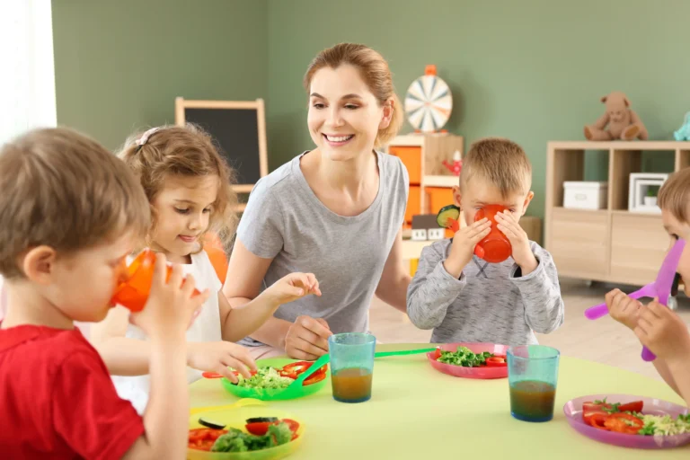 kindergarten teacher and group of young kids having vegetables for lunch at table