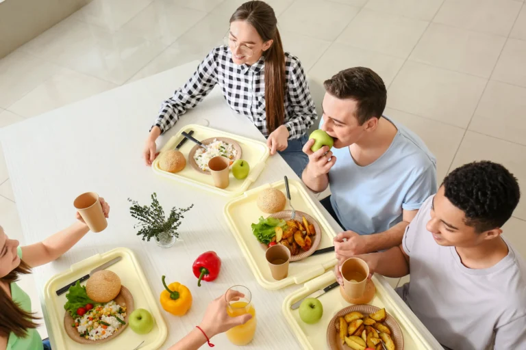group of young people having lunch on food trays in canteen